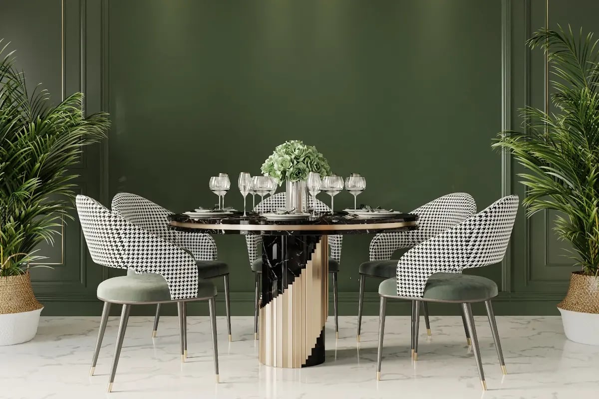Okrągły stół z czarnym blatem oraz czterema krzesłami. Stół jest zastawiony talerzami oraz kieliszkami. Ciemnozielona ściana.