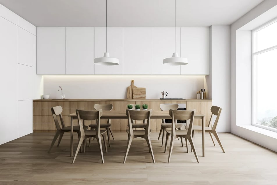 Kuchnia połączona z jadalnią. Meble z białymi frontami oraz w kolorze drewna oraz drewniany stół i krzesła w aranżacji stylu skandynawskiego.
