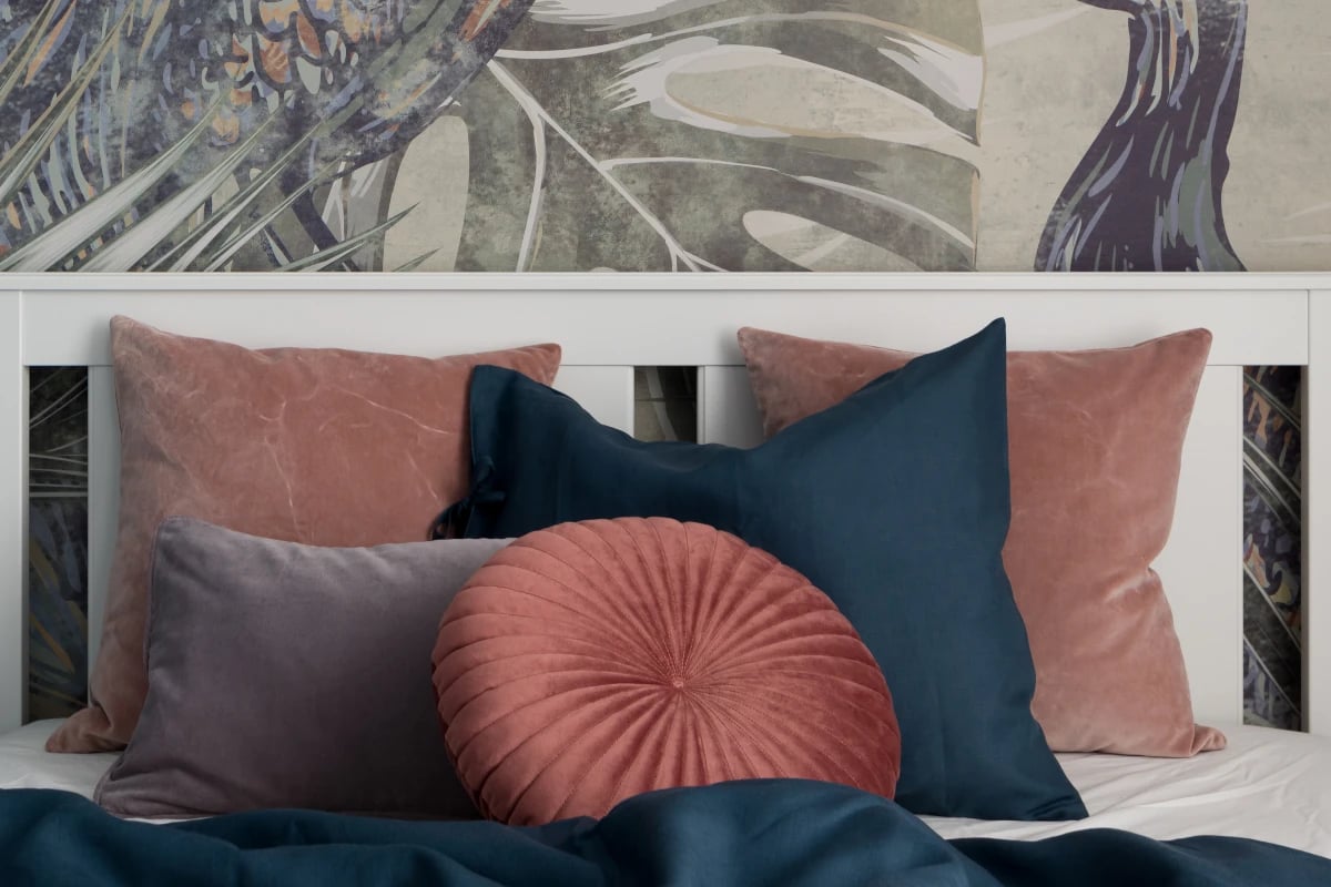 Poduszki kolorowe na łóżku. Na ścianie za łóżkiem tapeta ze wzorami roślinności. 