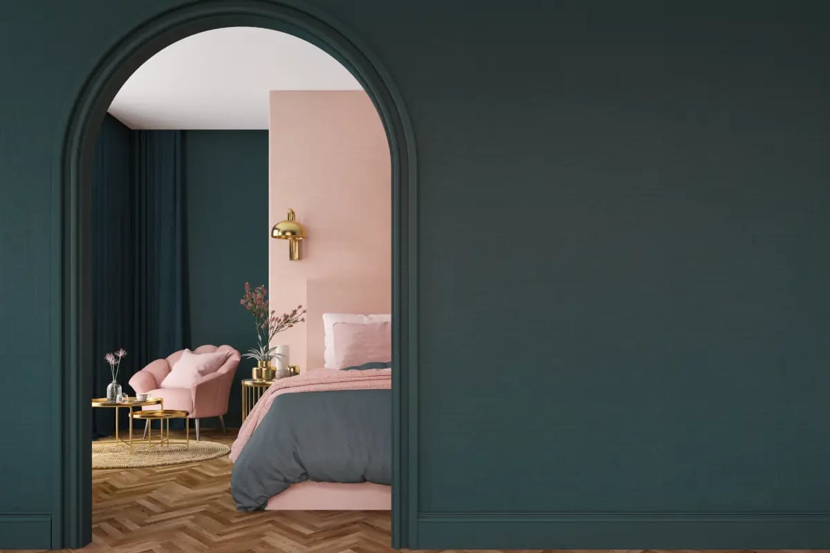 Ciemnozielona ściana z przejściem do kolejnego pomieszczenia. W tle widać łóżko oraz fotel oraz różową ścianę.