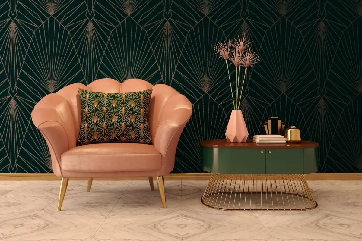 Różowy fotel z poduszką we wzory. Stolik z wazonem stoi obok. Ściana ciemnozielona we wzory. 