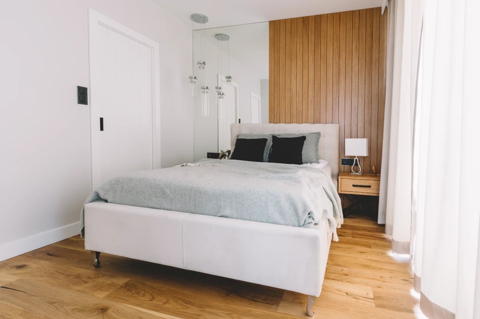 Duże łóżko w małej sypialni. Połączenie bieli i jasnych kolorów w zestawieniu z drewnem.