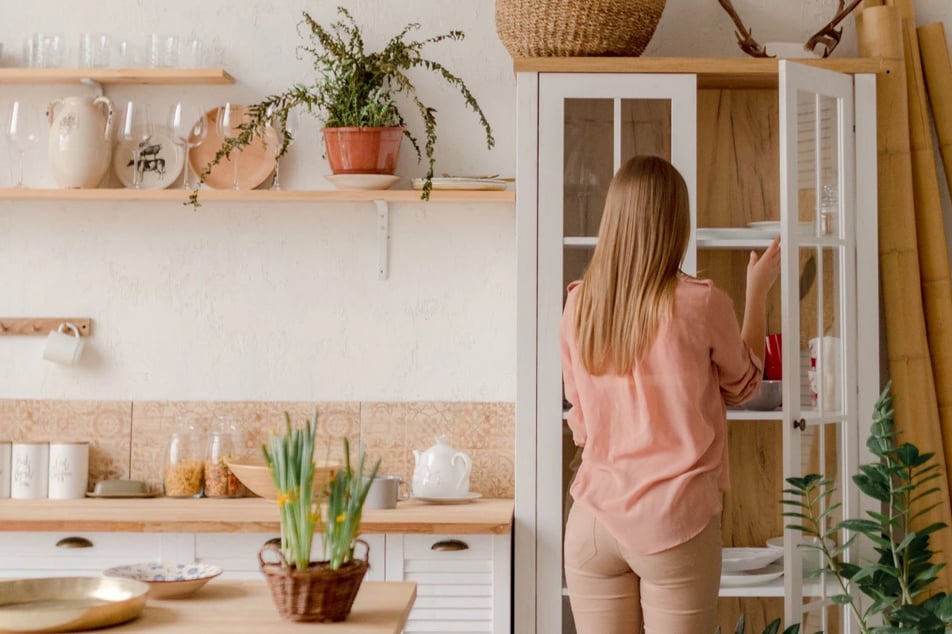 Kobieta wyciągająca talerze z witryny w kuchni urządzonej w stylu boho.