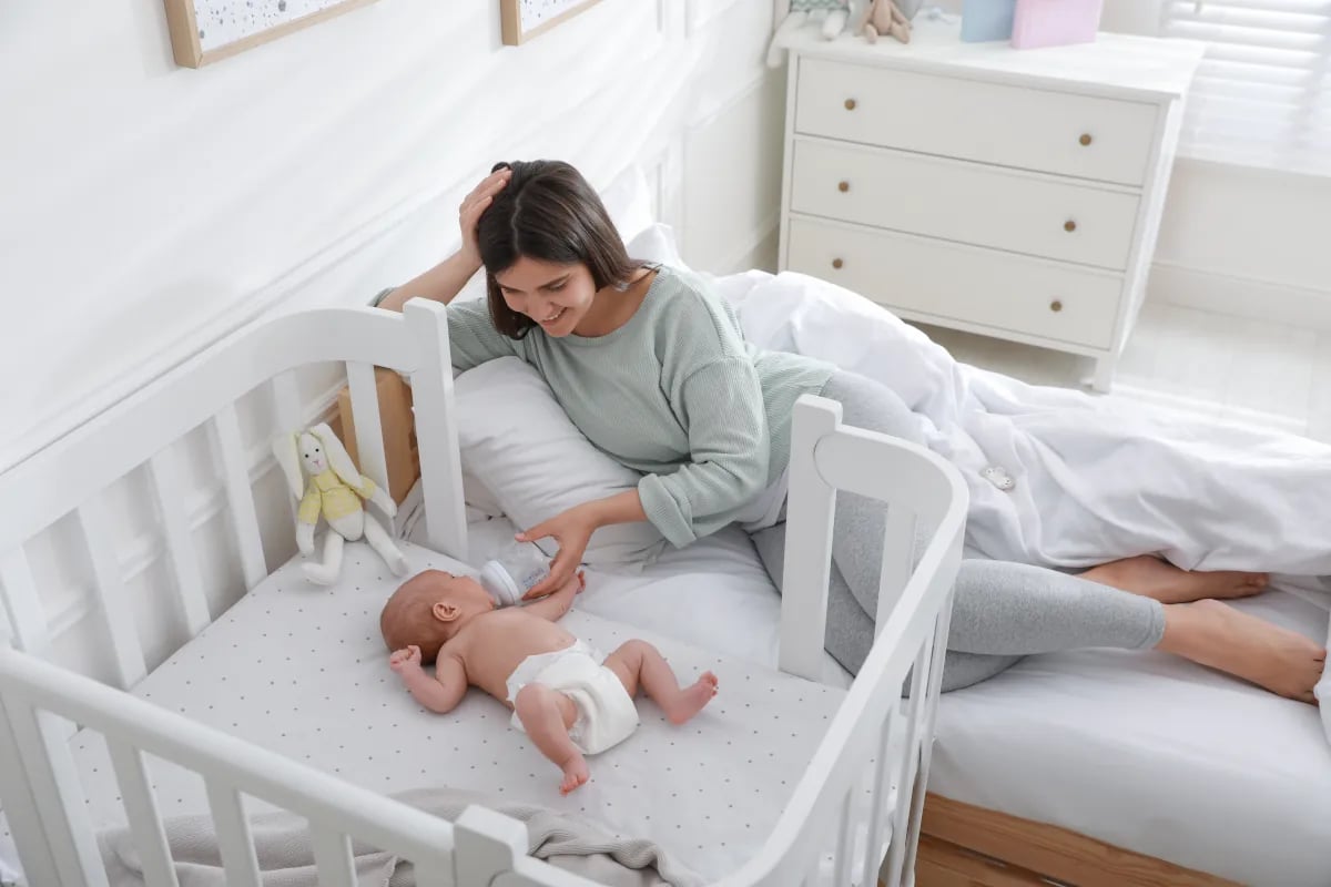 Mama leżąca na łóżku i karmiąca dziecko w dostawce.