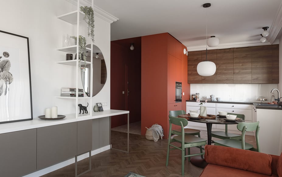 Wnętrze mieszkania ze stołem, kuchnią i salonem w białych i czerwonych barwach.