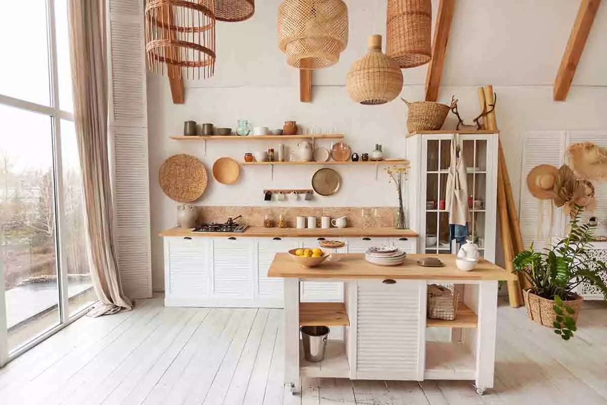 Kuchnia z dużym oknem. Meble kuchenne w połączeniu bieli oraz drewna. Duża ilość dekoracji oraz akcesoriów w stylu rustykalnym.