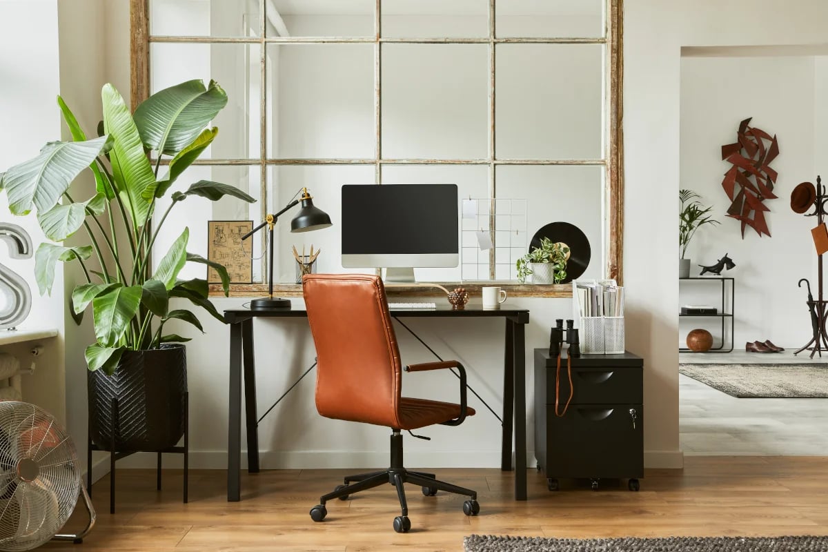 Wydzielone miejsce do pracy przy oknie. Biurko z monitorem oraz skórzany fotel. 