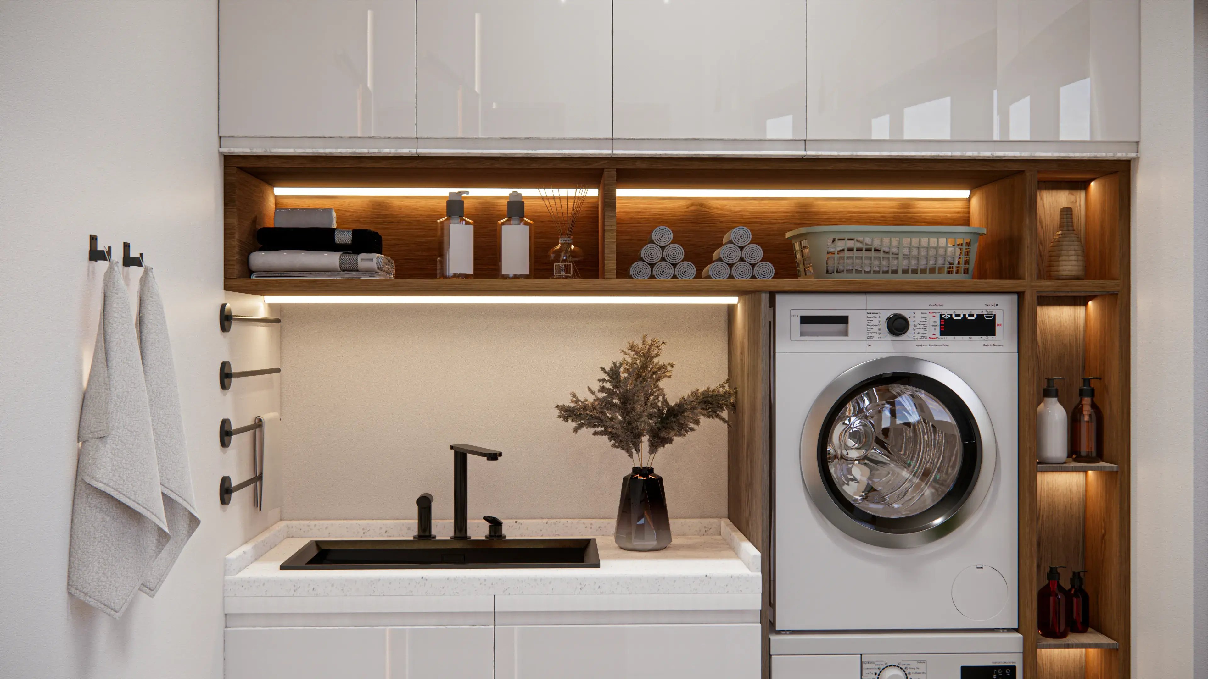 Pralnia w stylu skandynawskim z białymi szafkami dolnymi i wiszącymi, drewnianymi niewielkimi regałami pod szafkami, umywalką i dwoma pralkami stojącymi obok zabudowanymi regałami. 