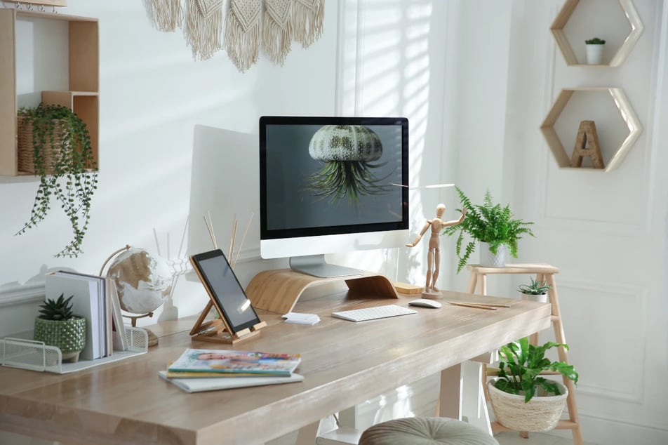 Biurko w kolorze drewna. Na biurku stojący monitor, globu, figura człowieka, roślinne i inne dodatki.