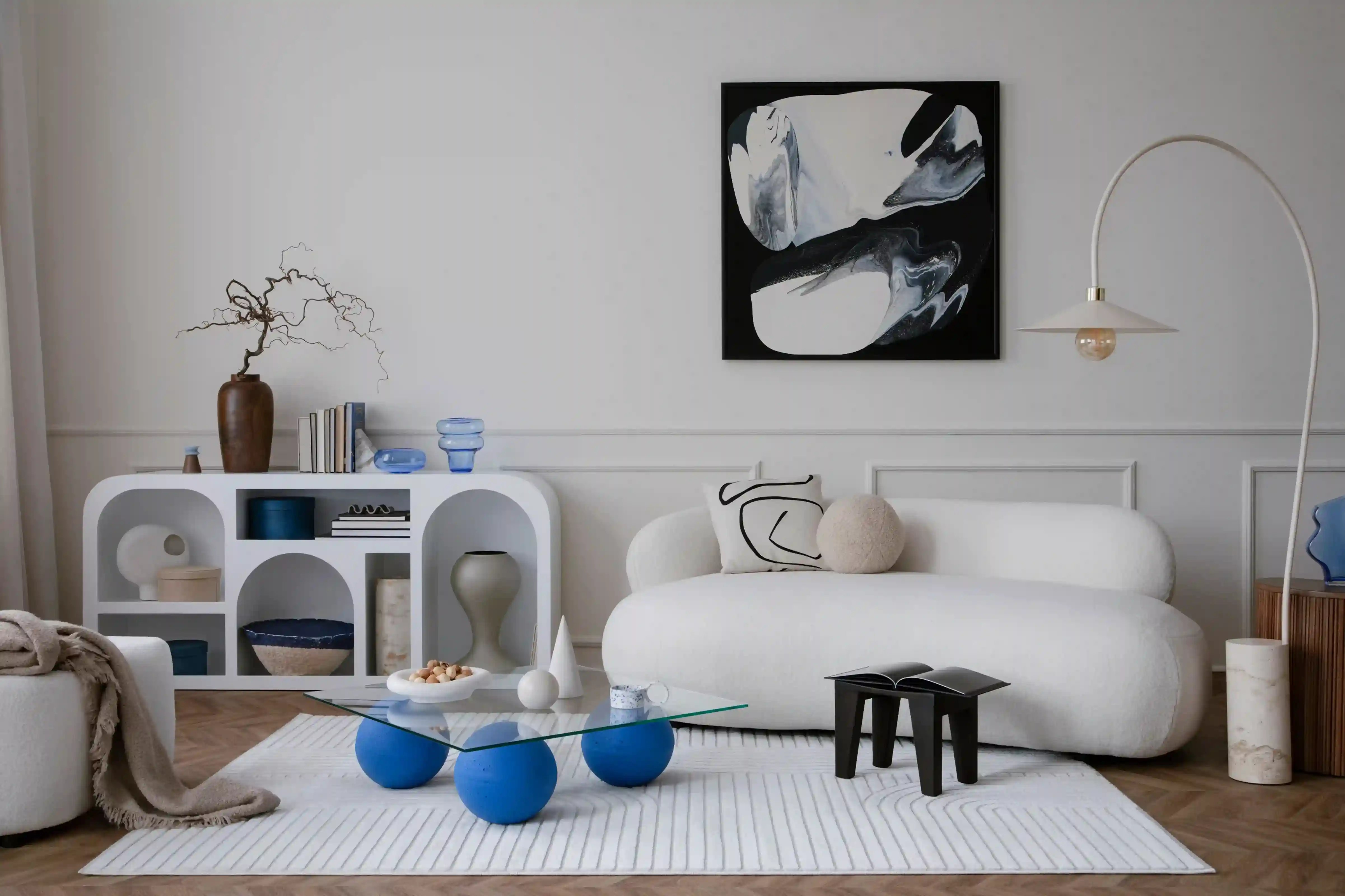 Skandynawski salon z białą kanapą i regałem oraz szklanym stolikiem. Nad kanapą wisi abstrakcyjny obraz.