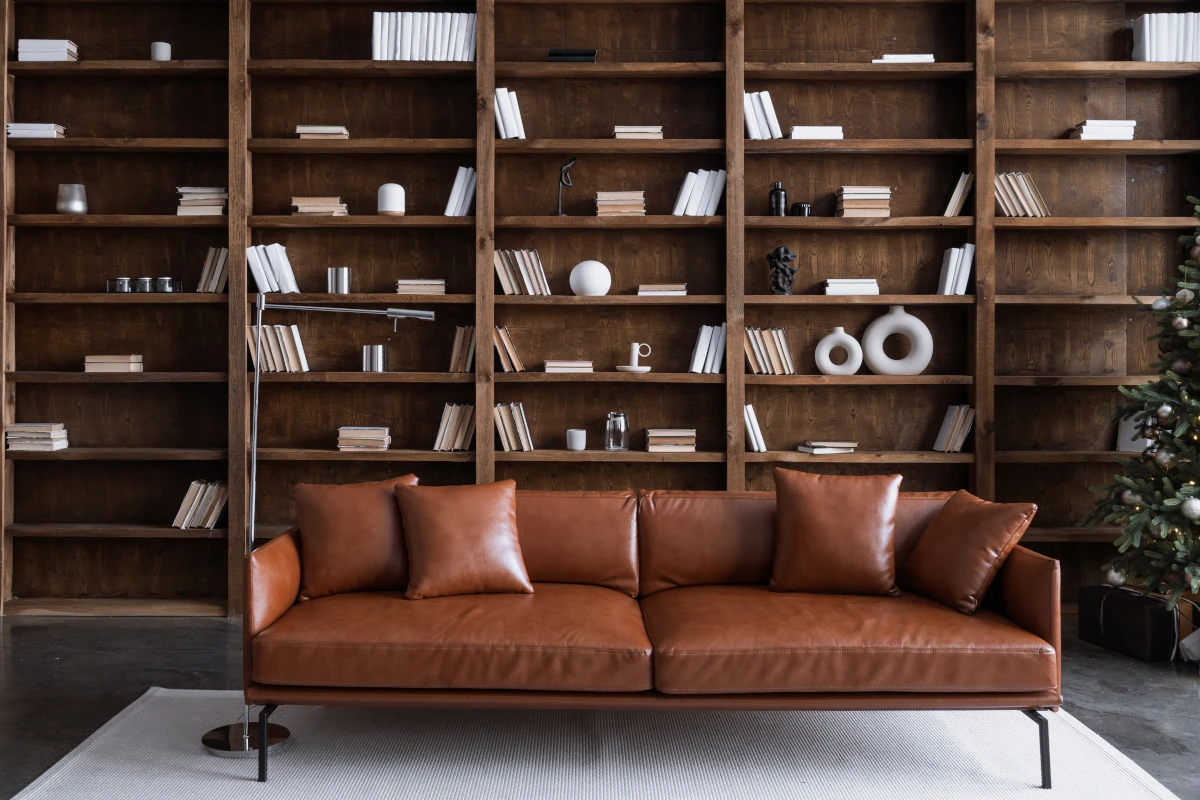 Brązowa skórzana sofa stojąca na tle brązowych regałów z książkami.