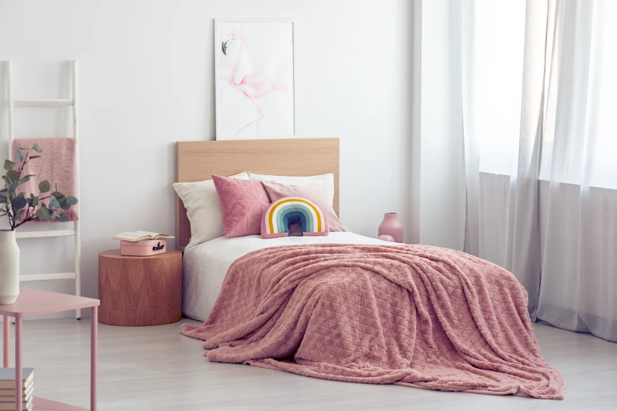 Łóżko z narzutami oraz poduszkami w kolorze różu. Na ścianie nad łóżkiem obraz.