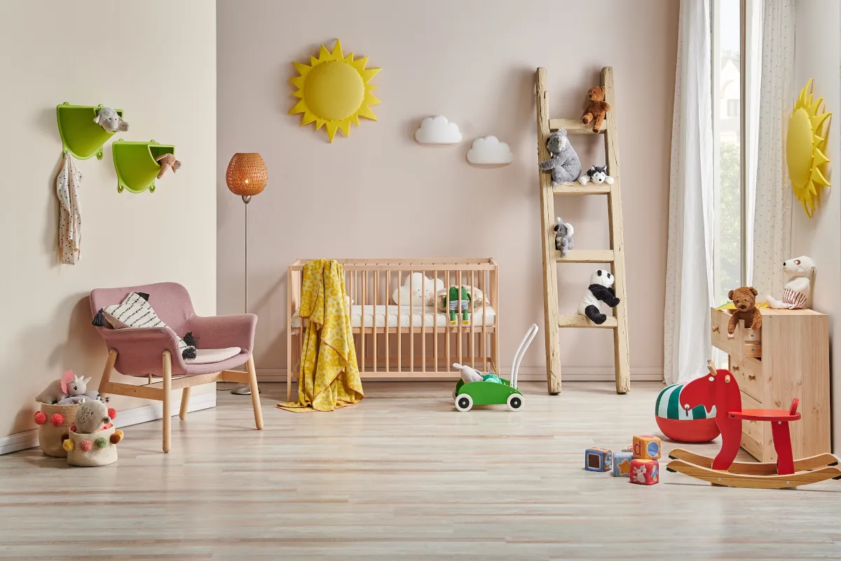 Pokój dla noworodka z łóżeczkiem oraz fotelem. Na ścianie dekoracje w postaci słońca oraz chmur. Dużo zabawek na podłodze.